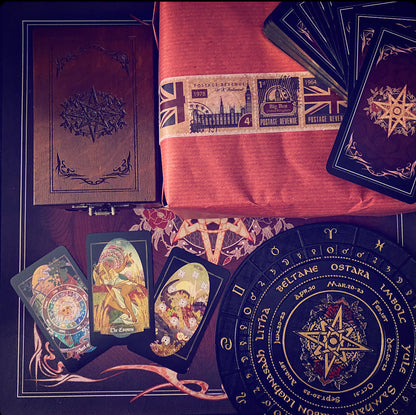A styled flat-lay of tarot card and occult-themed items on a dark surface: a brown embossed book or journal, a folded orange-red cloth with vintage stamps, a stack of dark tarot cards, several illustrated cards, and a large circular black pentagram wheel with gold text and symbols.