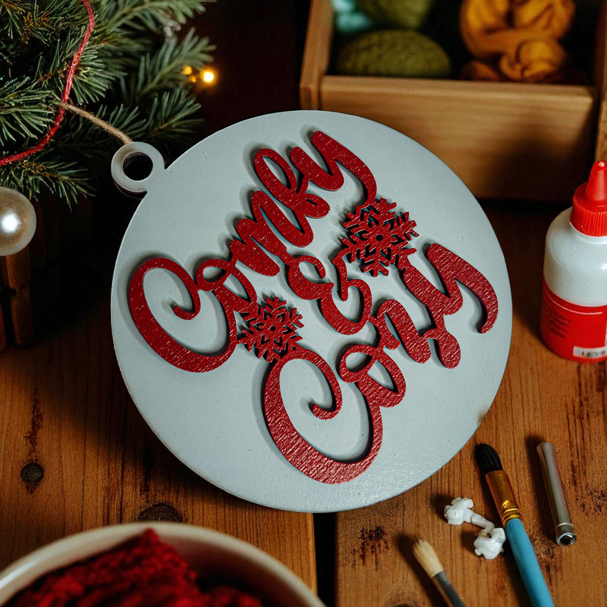Decorative ornament with 'Merry Christmas' text on a wooden surface with crafting supplies.