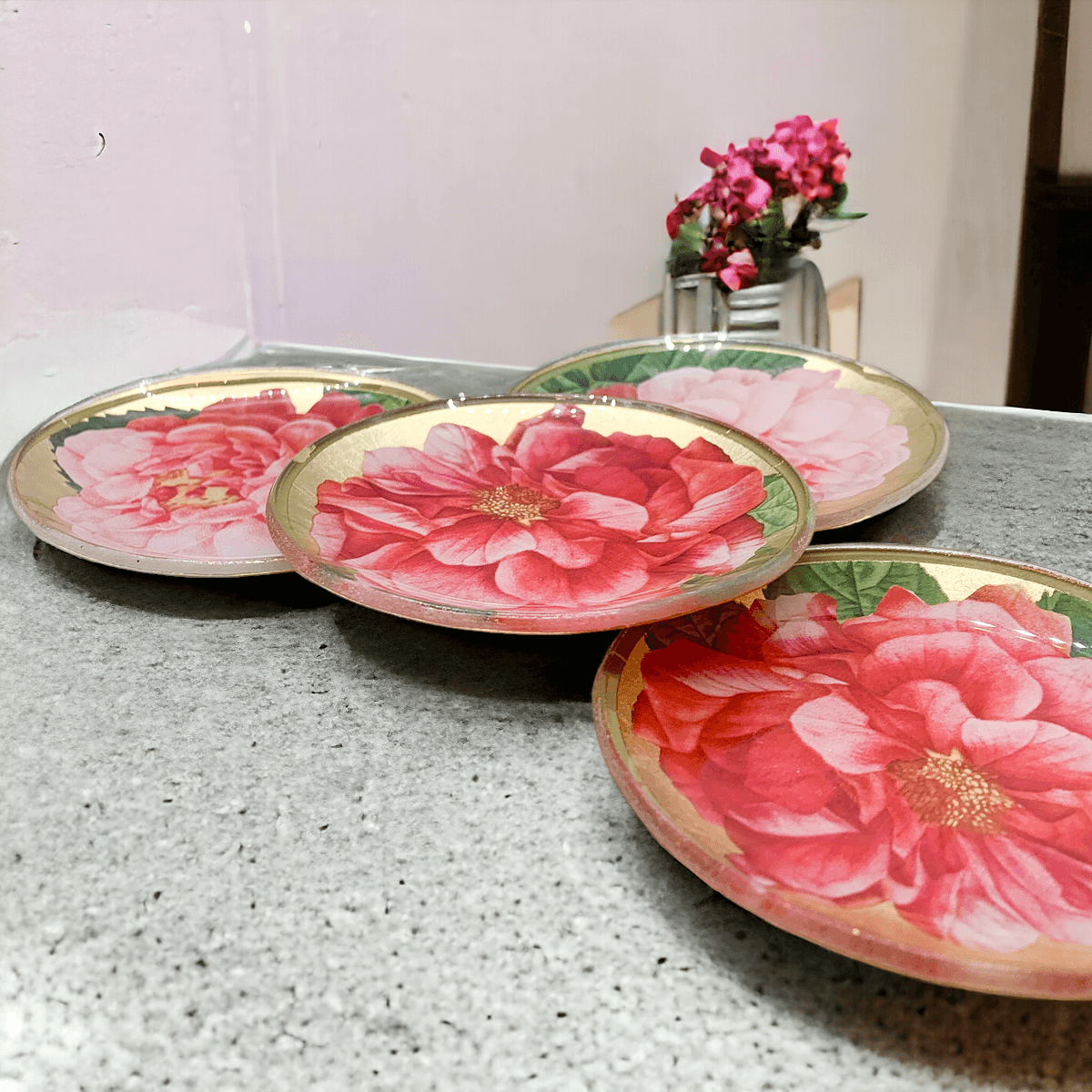 Set of three decorative plates with pink floral designs on a gray surface.