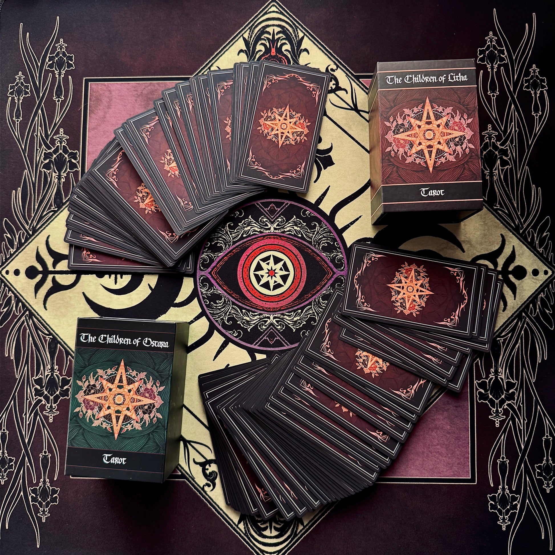 A set of tarot cards from 'The Children of Osiris' deck arranged in a flat-lay on a matching decorative tarot mat. The cards are fanned out and stacked, showing dark maroon backs with gold star illustrations, alongside two boxed decks, one with a green cover and one with a dark red cover.