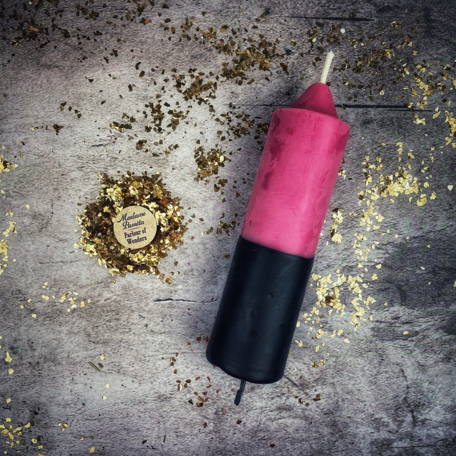 Pink and black candle on a textured surface with gold confetti
