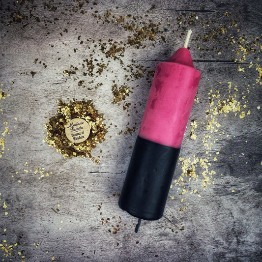 Pink and black candle on a textured surface with gold confetti