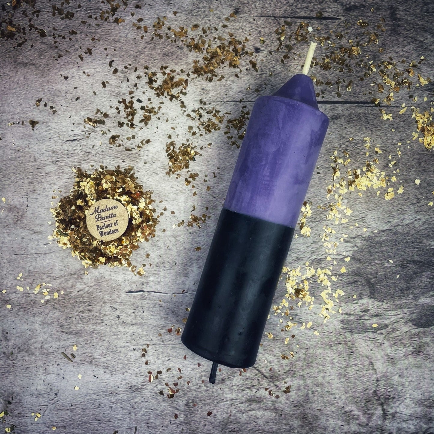 Purple and black candle on a textured surface with gold confetti