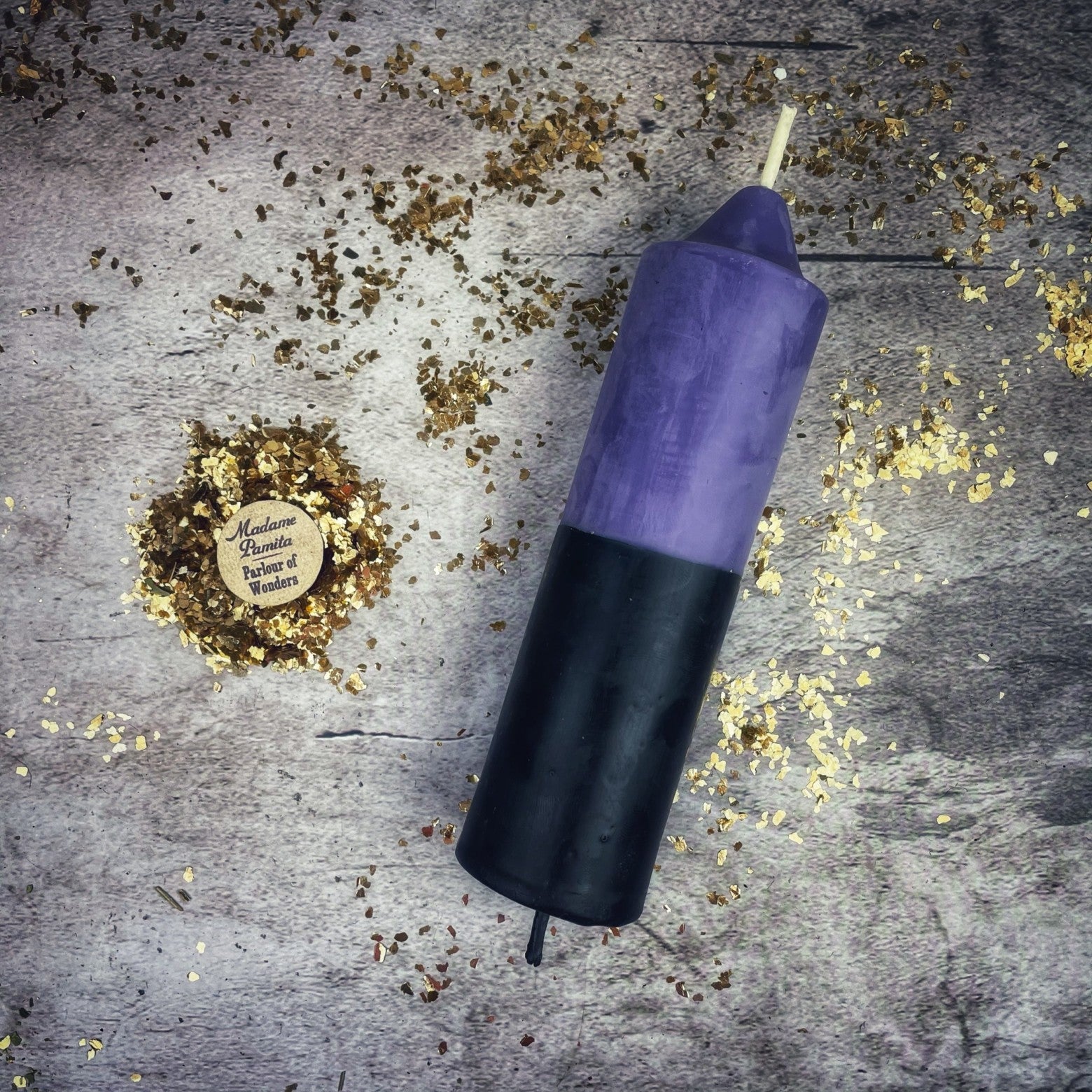 Purple and black candle on a textured surface with gold confetti