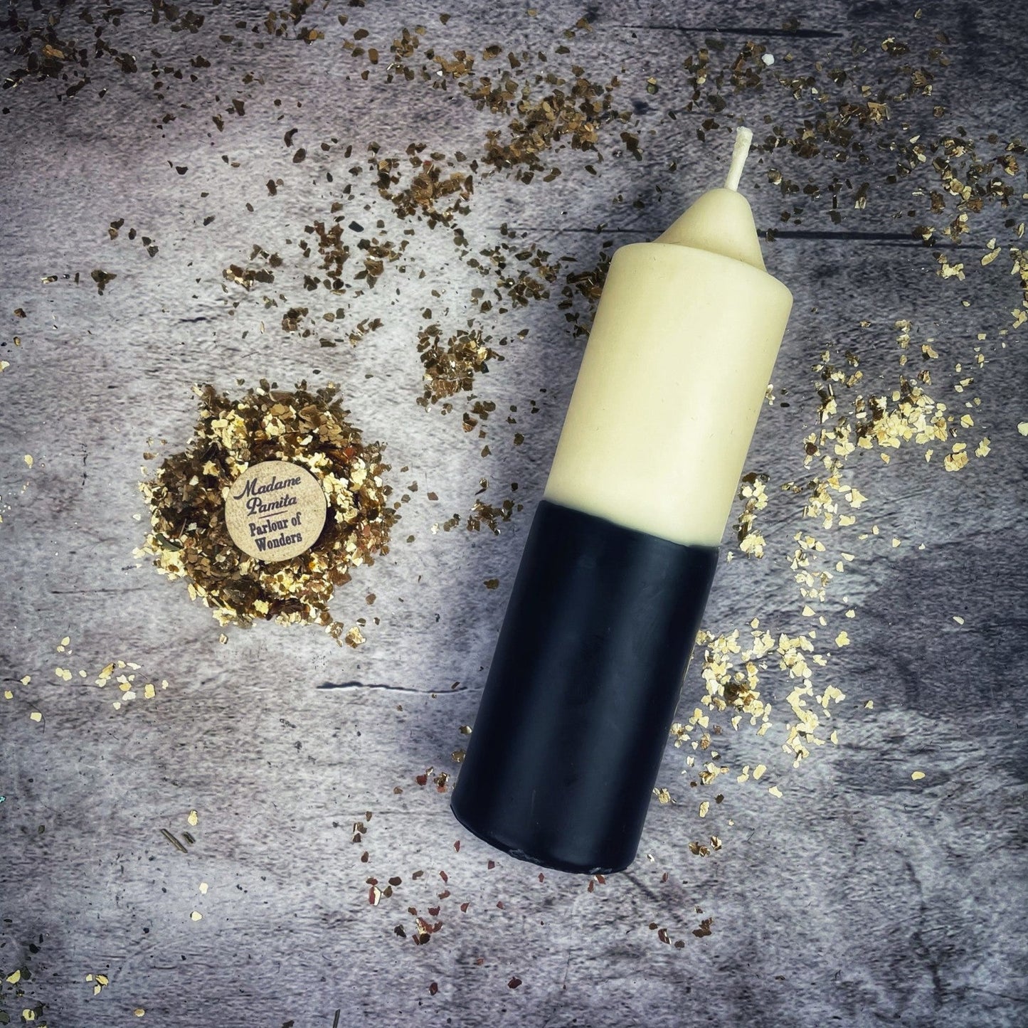 Candle with black base and white top on a textured surface with gold confetti