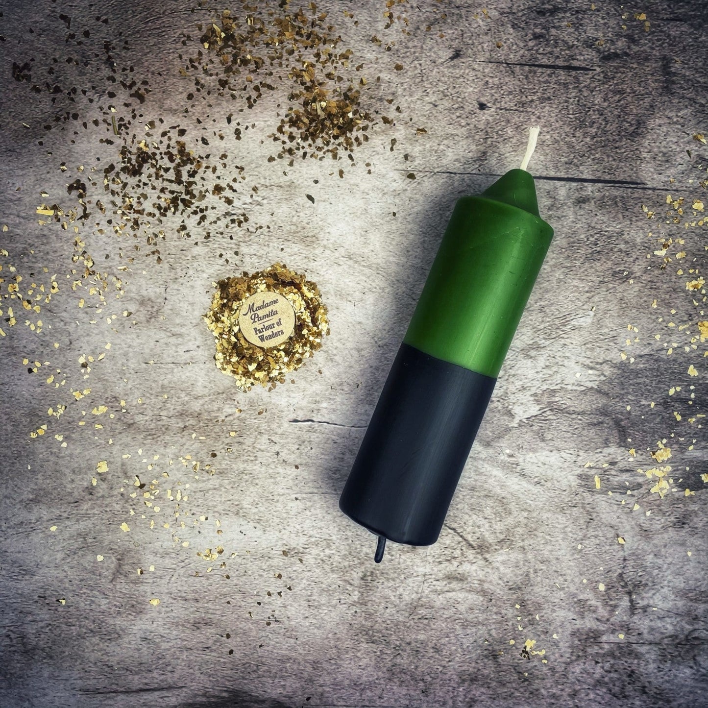 Green and black candle on a textured surface with gold confetti