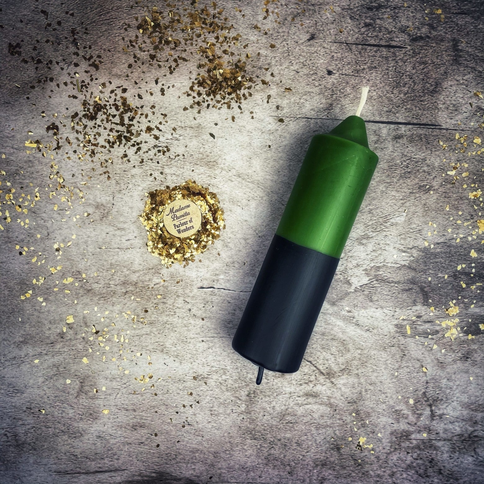 Green and black candle on a textured surface with gold confetti