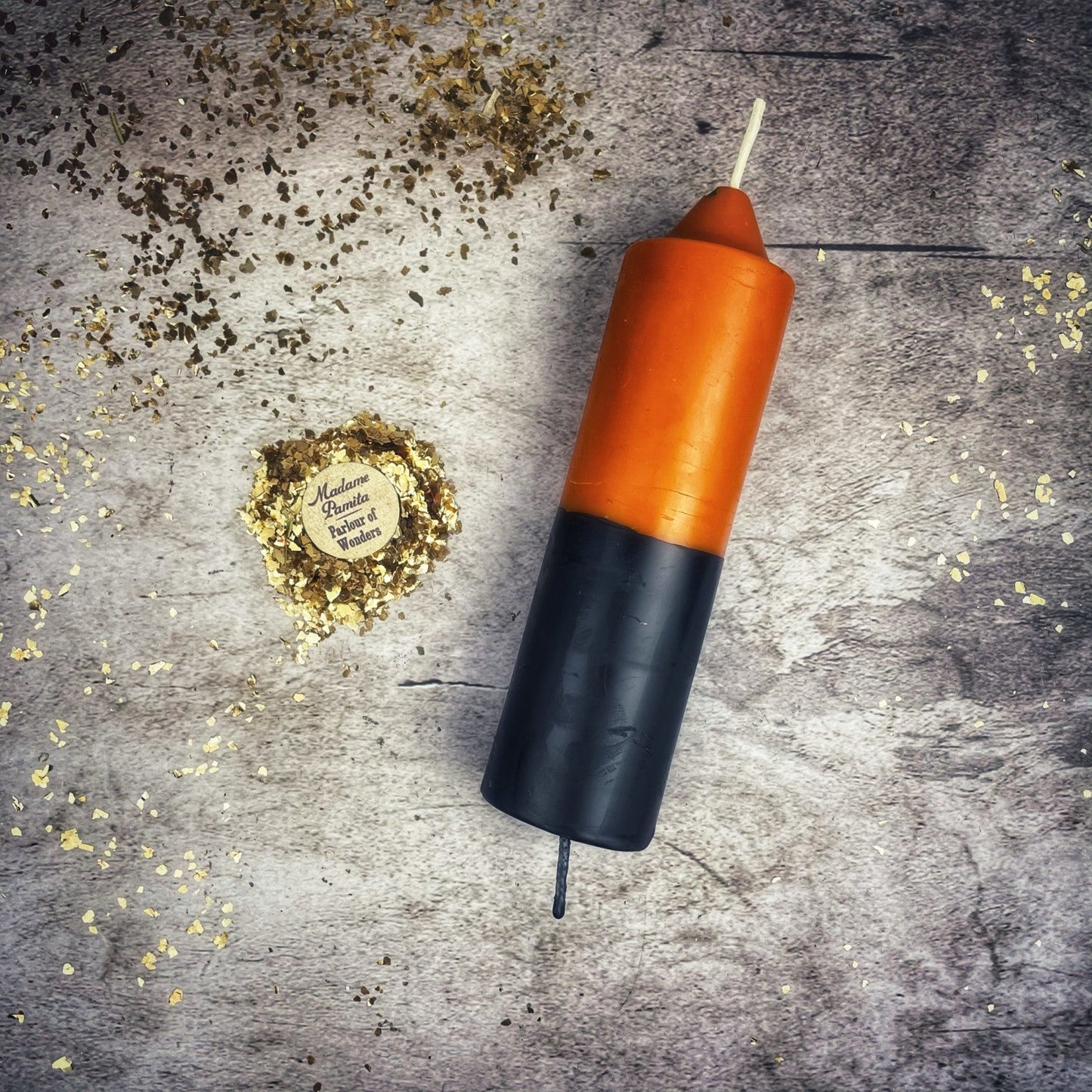 Black and orange candle on a textured surface with gold confetti