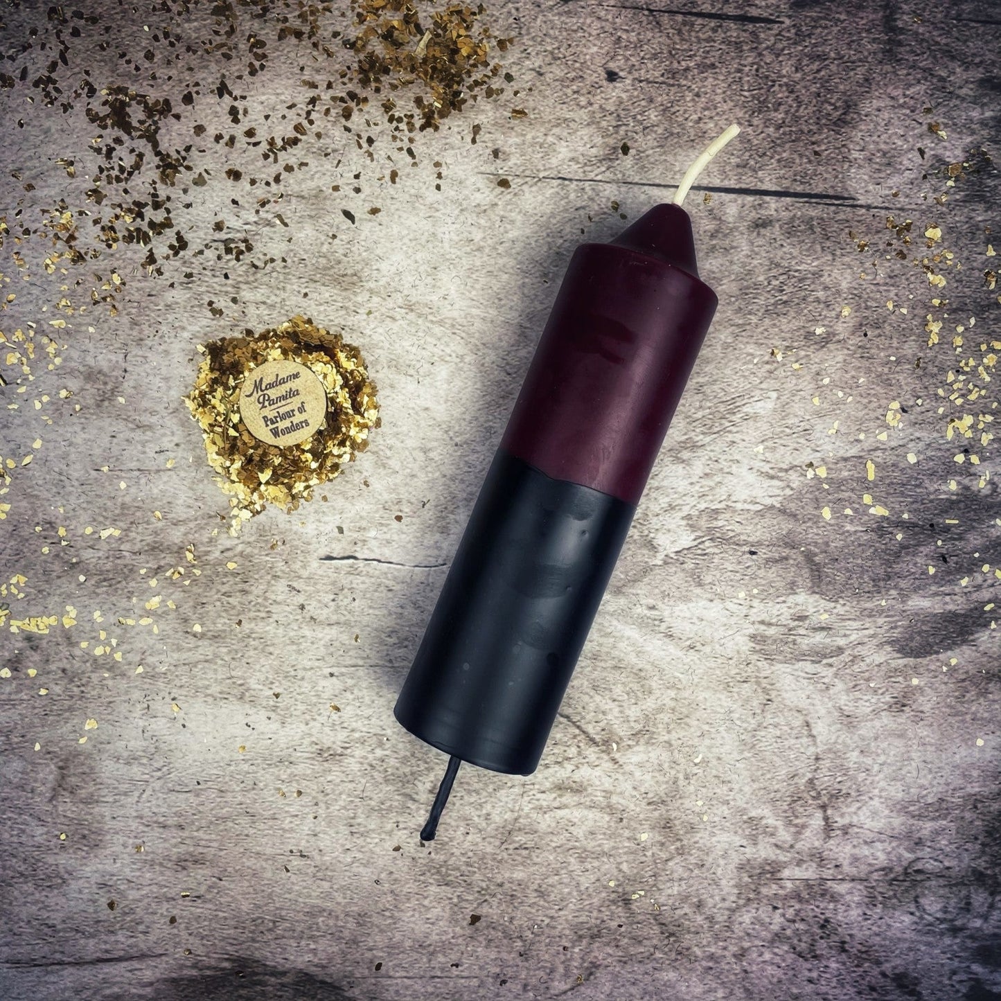 Candle with a black base and red top on a textured surface with gold confetti.