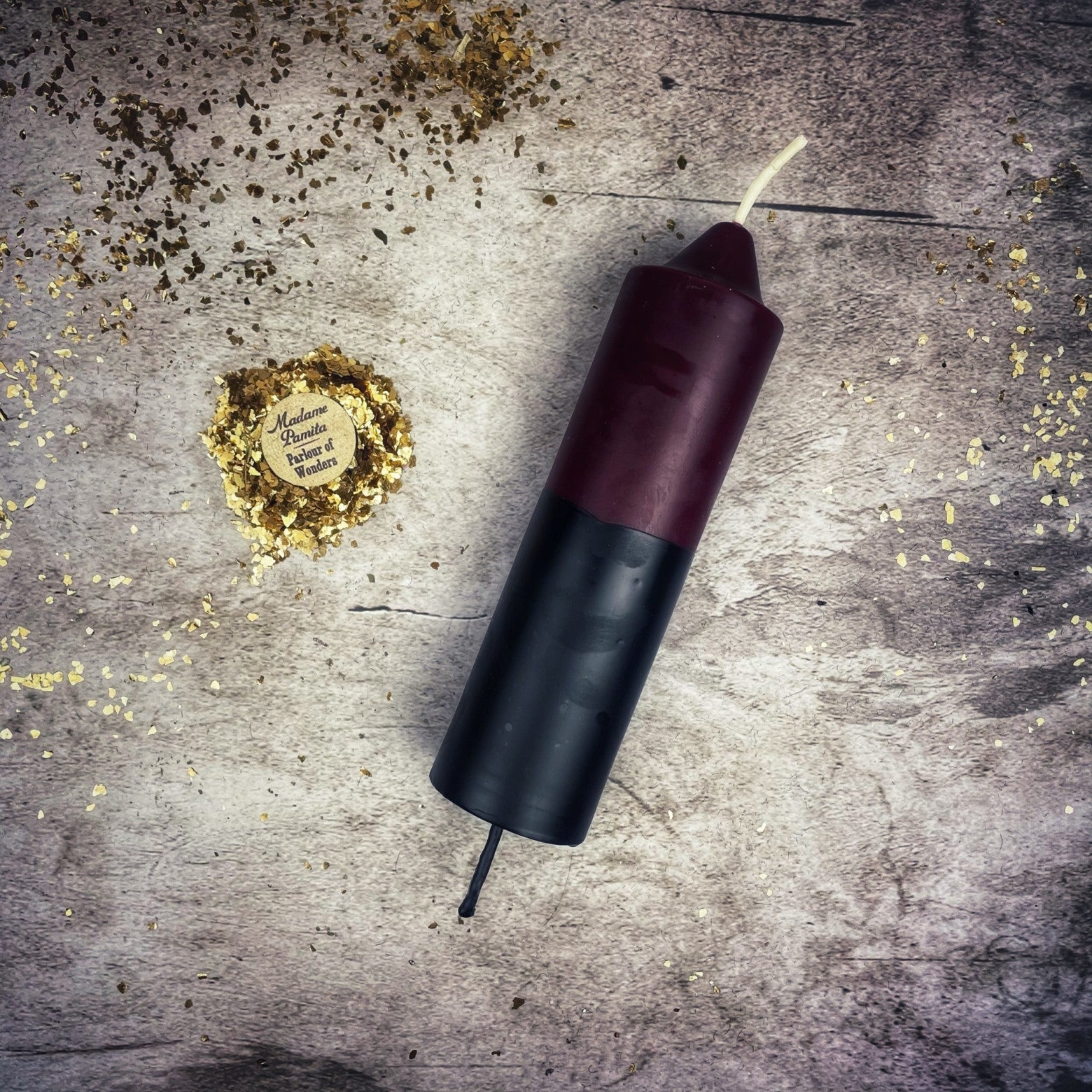 Candle with a black base and red top on a textured surface with gold confetti.
