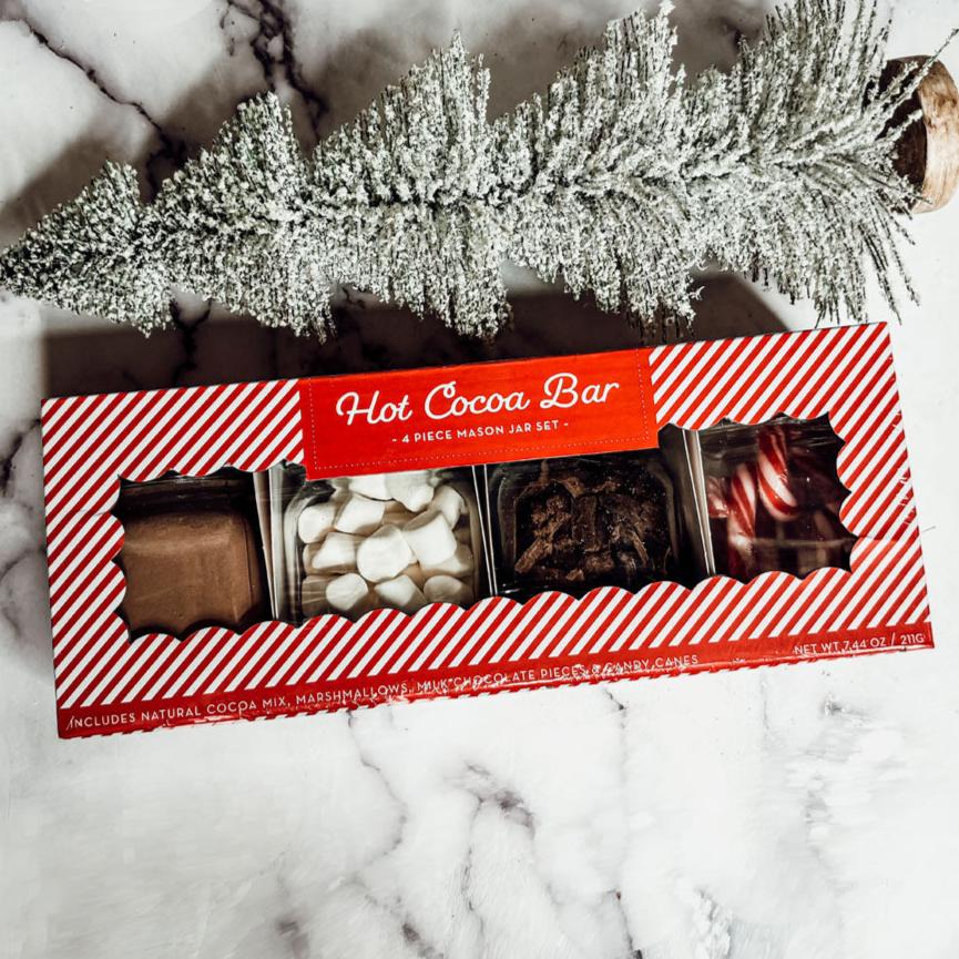 Hot cocoa bar set packaging on a marble surface with decorative branches.