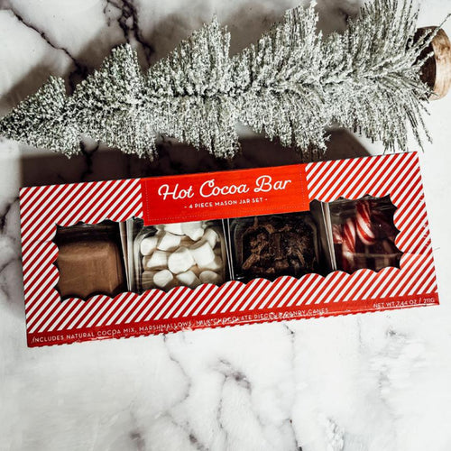 Hot cocoa bar set packaging on a marble surface with decorative branches.