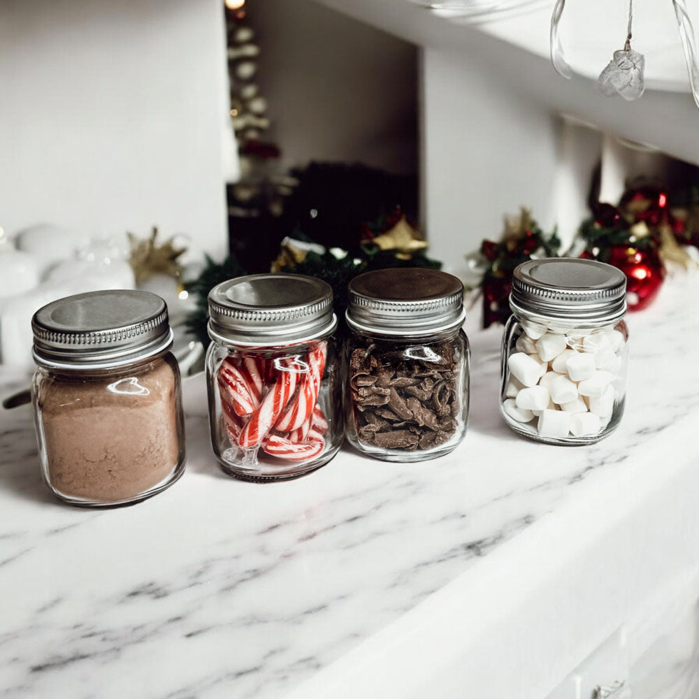 Four mason jars with silver lids on a marble surface, containing different items.
