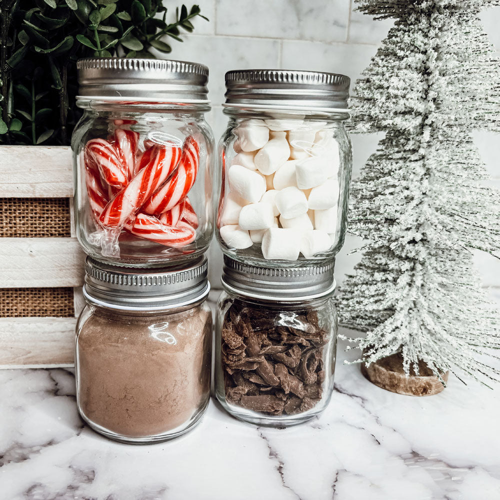 Stack of glass jars with festive contents on a marble surface with Christmas decorations.