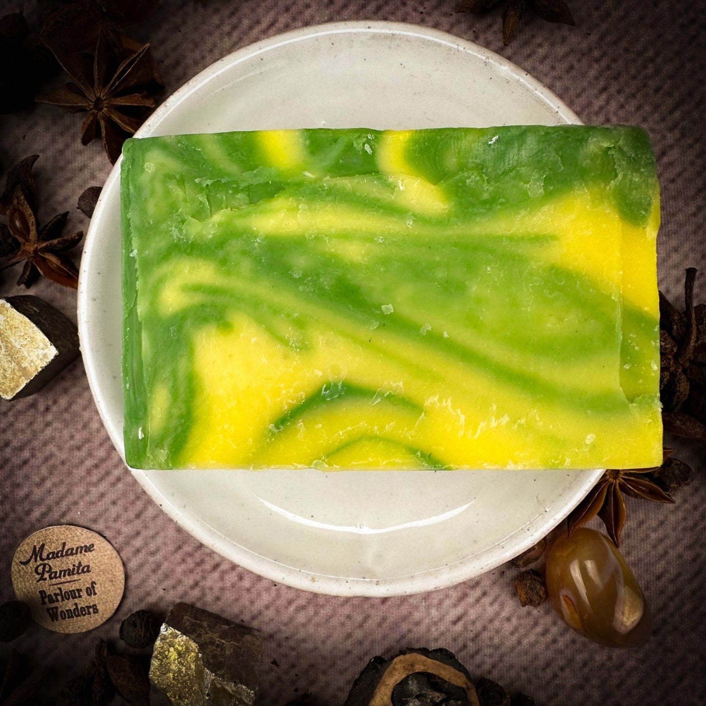 Green and yellow marbled soap bar on a white plate with star anise and other spices in the background.