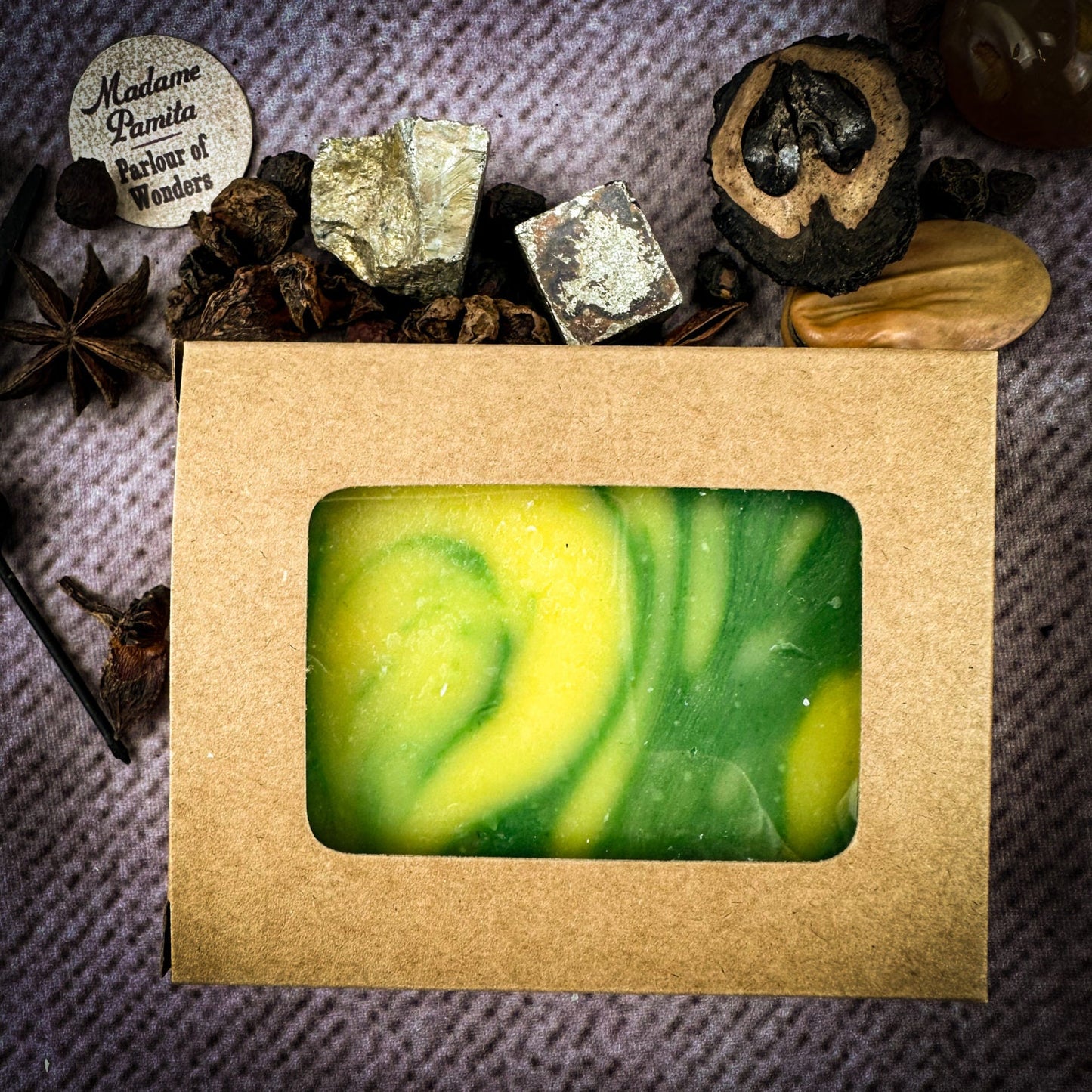Green and yellow swirled soap bar in a brown cardboard box with decorative elements on a textured surface.