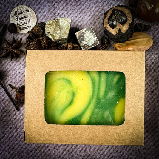 Green and yellow swirled soap bar in a brown cardboard box with decorative elements on a textured surface.