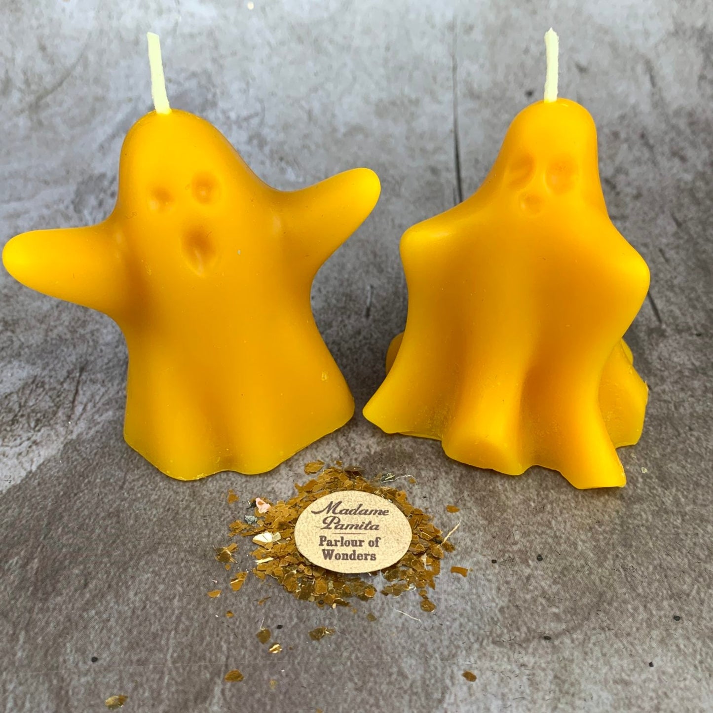 Two yellow ghost-shaped candles on a gray surface with a branded logo.