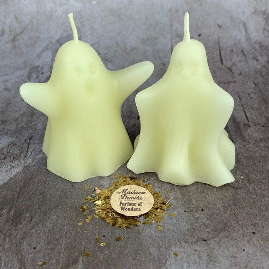 Two ghost-shaped candles on a textured surface with a small round label.
