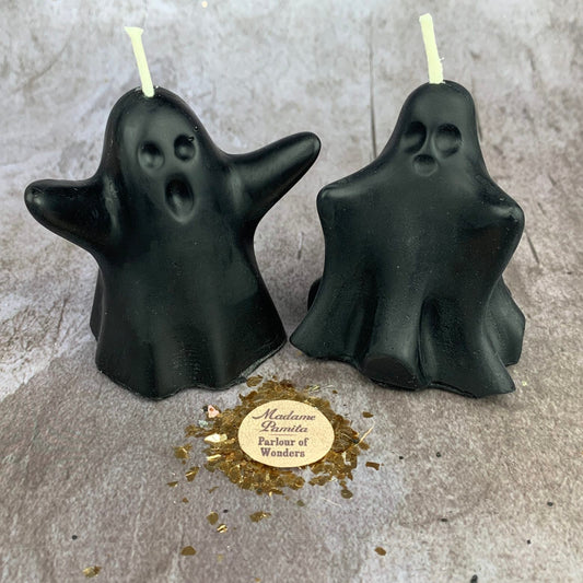 Two black ghost-shaped candles on a gray surface with a gold label.