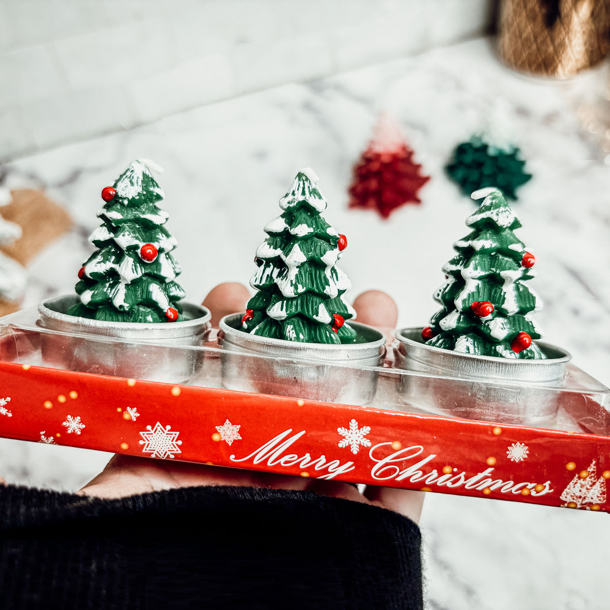 Three small Christmas tree figurines in a decorative box with 'Merry Christmas' text.