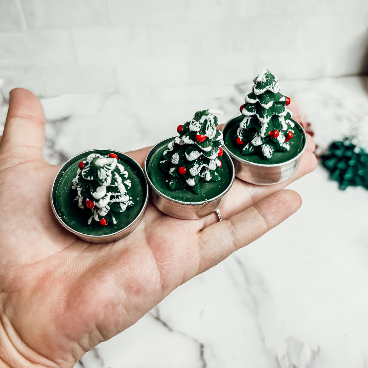 Hand holding three small Christmas tree-shaped containers with green and red decorations.