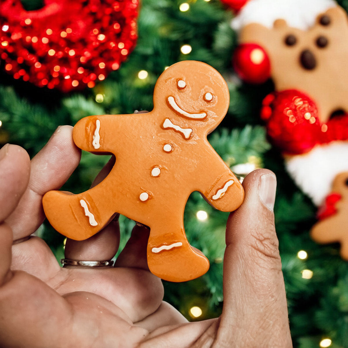 Hand holding a gingerbread man cookie with Christmas decorations in the background