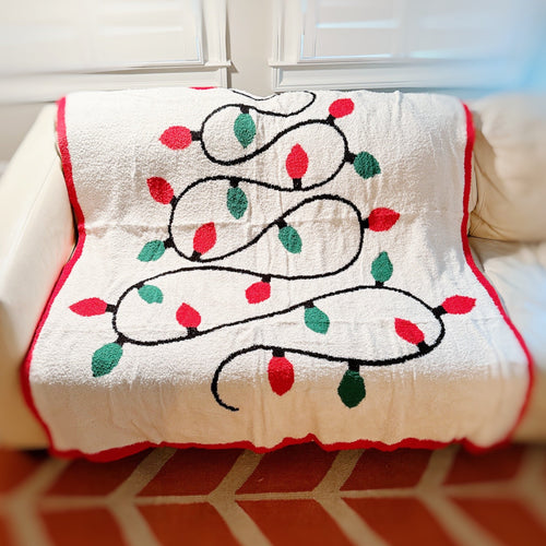 Decorative blanket with Christmas lights design on a couch.