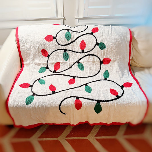 Decorative blanket with Christmas lights design on a couch.