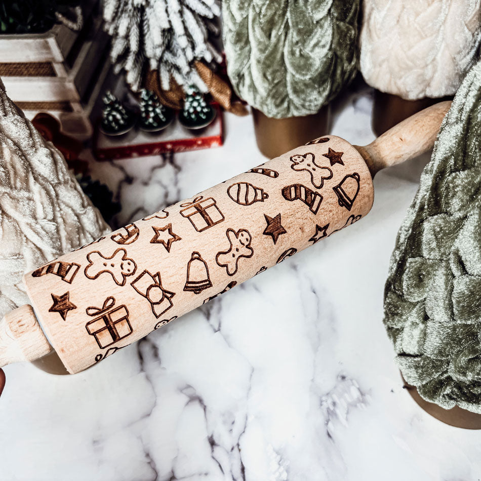 Wooden rolling pin with Christmas-themed designs on a marble surface