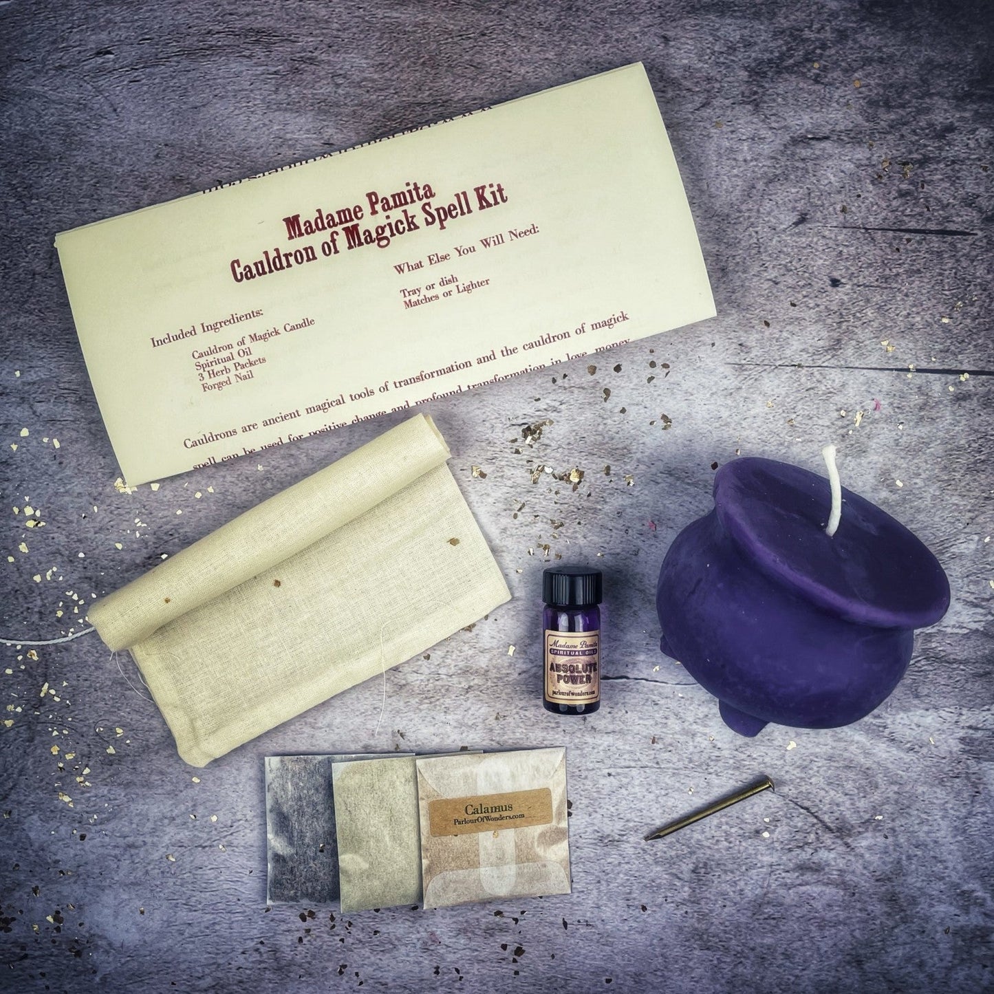 Magick spell kit with a purple cauldron, candle, and other items on a textured surface.