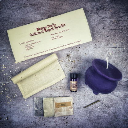 Magick spell kit with a purple cauldron, candle, and other items on a textured surface.