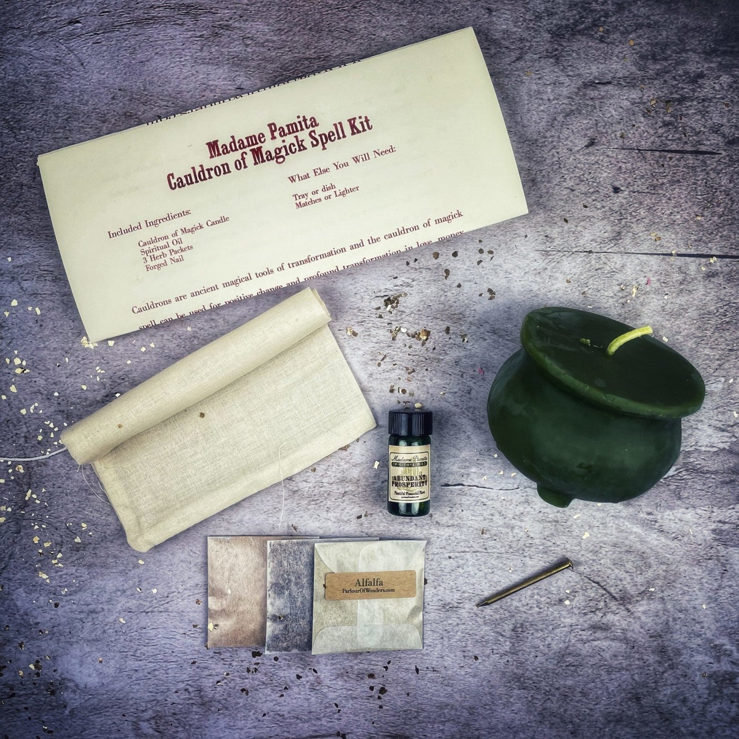 Magick spell kit with a green cauldron, scroll, and bottle on a dark surface