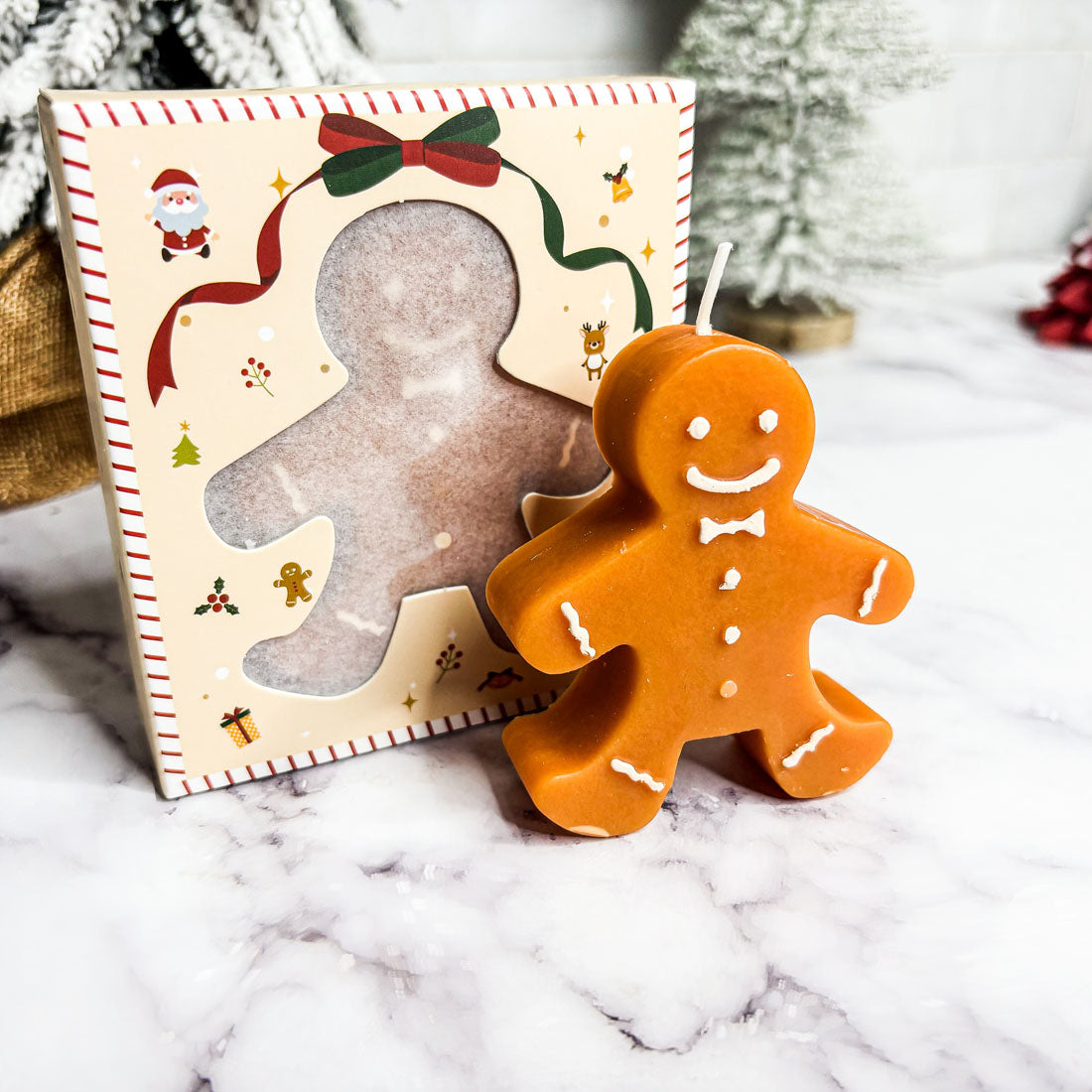 Gingerbread man candle next to a decorative gingerbread man card on a marble surface.