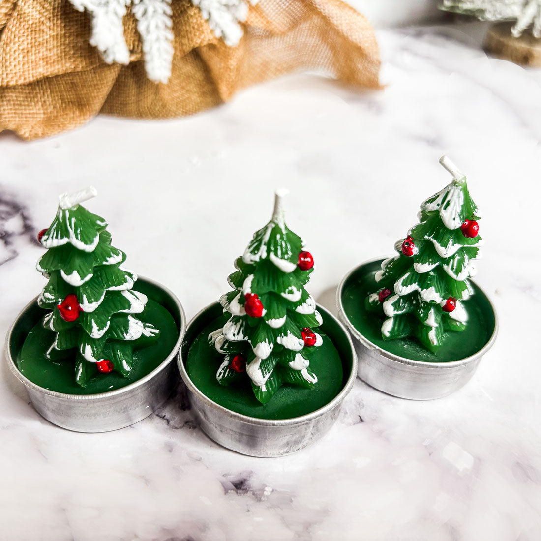 Three Christmas tree-shaped candles in metal holders on a marble surface.