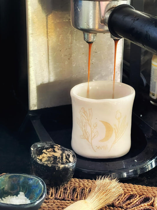 Espresso being poured into a white ceramic cup with decorative design on a black surface.