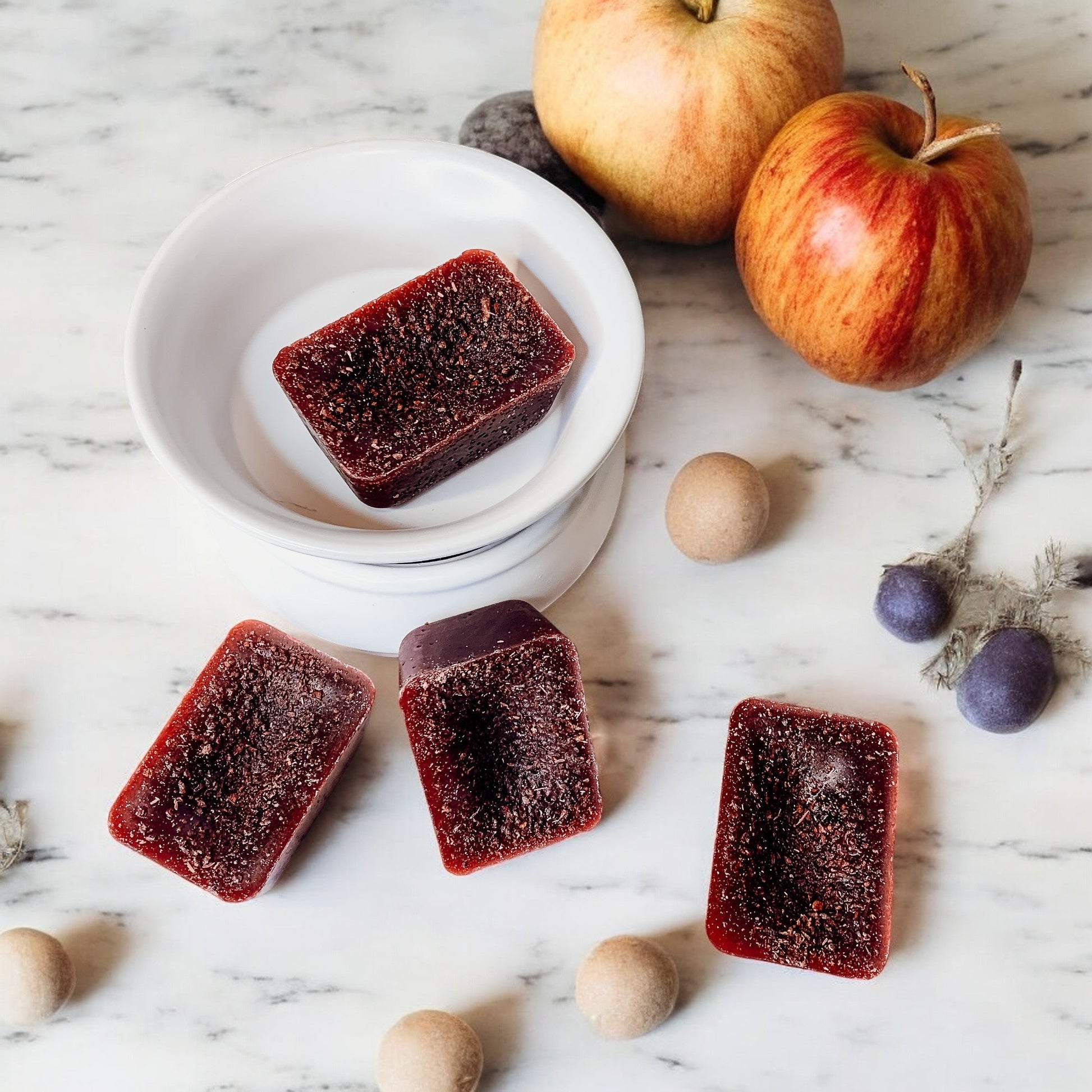 Red jelly squares on a marble surface with apples and small round objects.