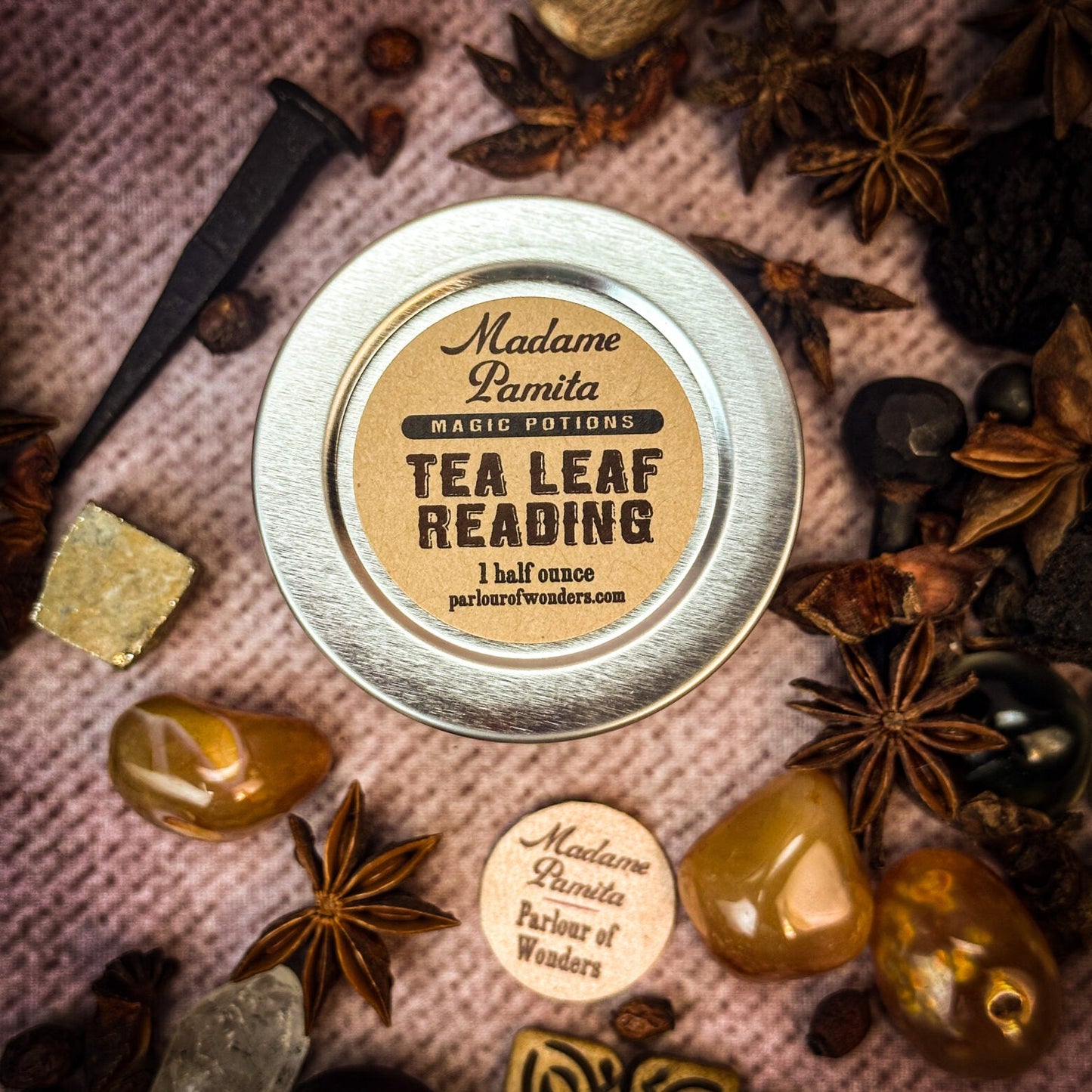Metallic tin labeled 'Tea Leaf Reading' surrounded by dried herbs and stones on a textured surface.