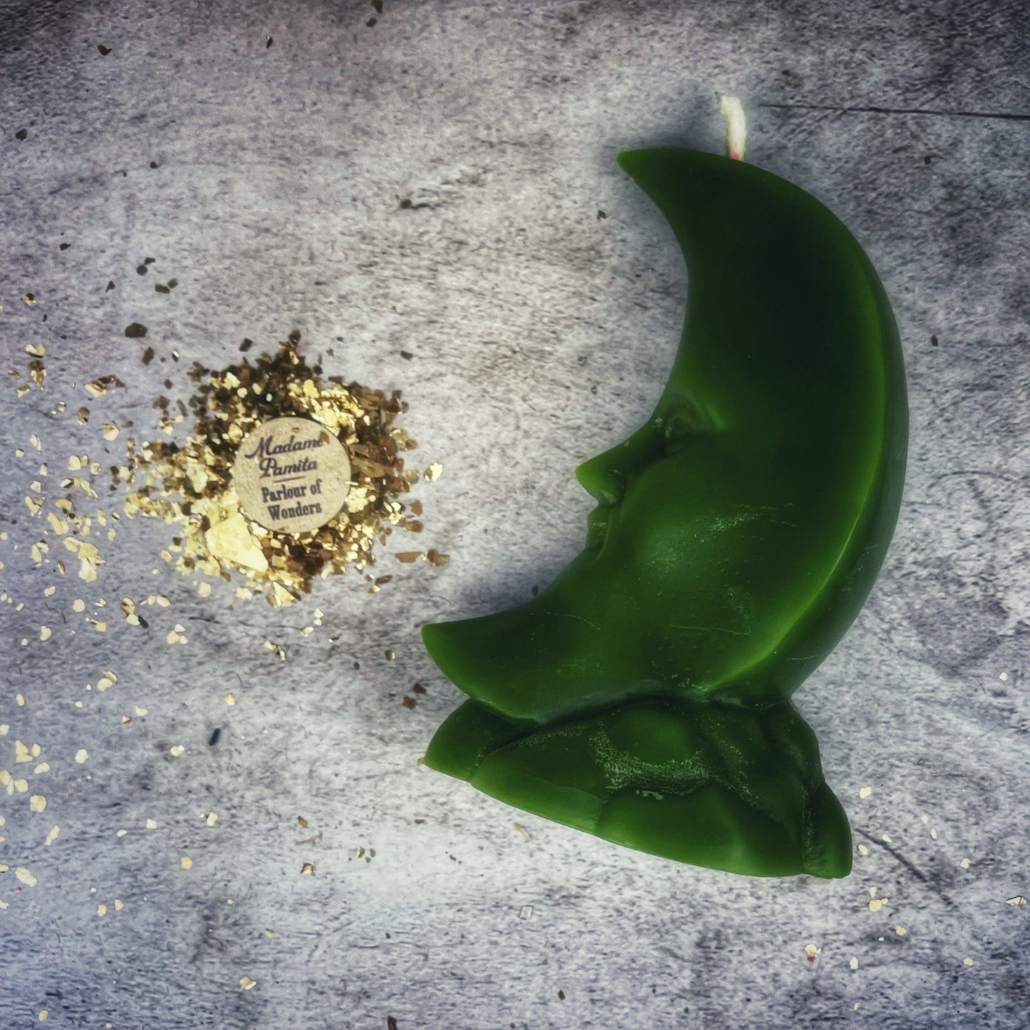 Green crescent-shaped candle on a textured surface with gold leaf and a label.