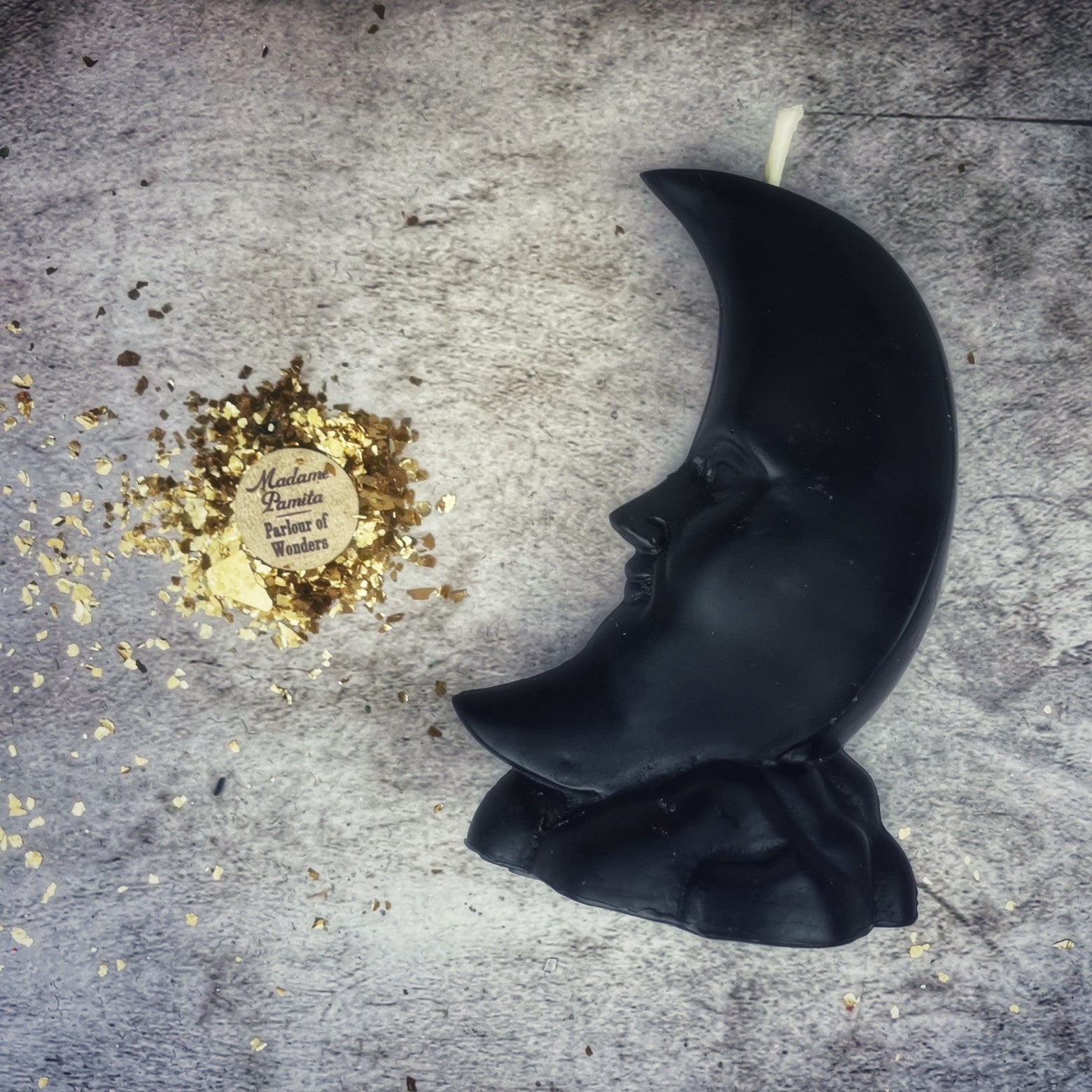 Black moon-shaped candle on a textured surface with gold leaf