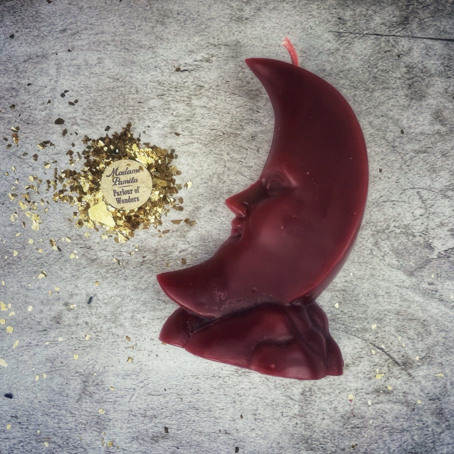 Red crescent moon-shaped candle on a textured surface with gold leaf