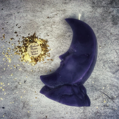 Purple crescent moon-shaped candle on a textured surface with gold confetti and a logo.