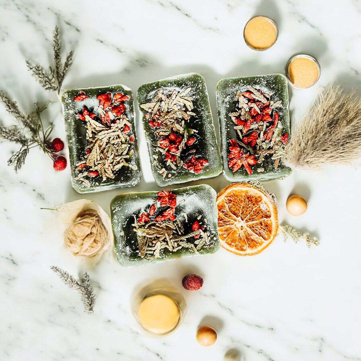 Four square containers with dried herbs and fruits on a marble surface with decorative elements.