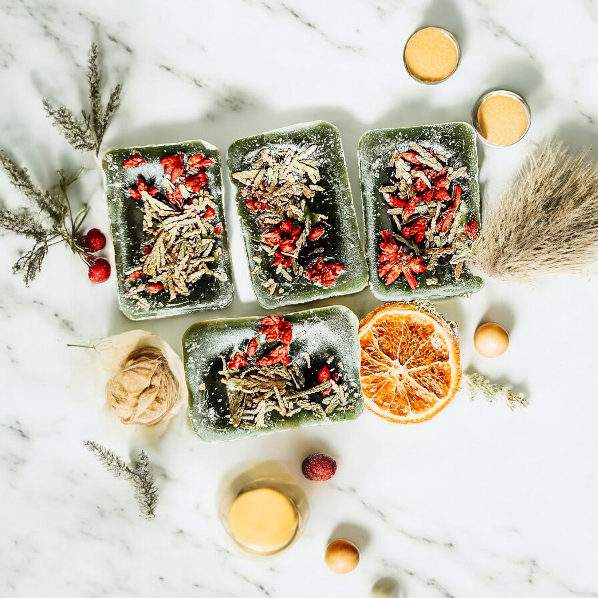 Four square containers with dried herbs and fruits on a marble surface with decorative elements.