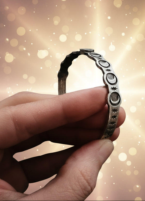 Hand holding a silver bracelet with star and moon designs against a dark background