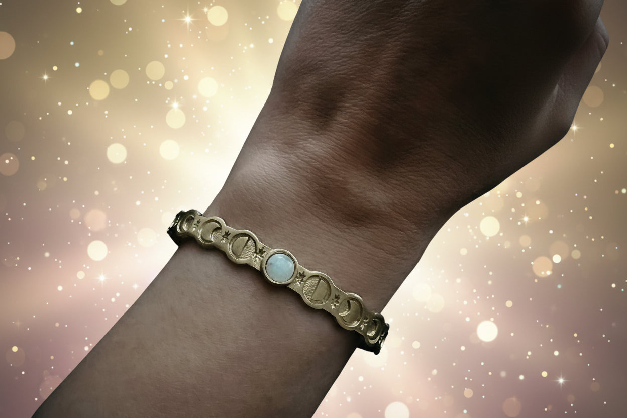Gold bracelet with a central gemstone on a wrist against a dark background