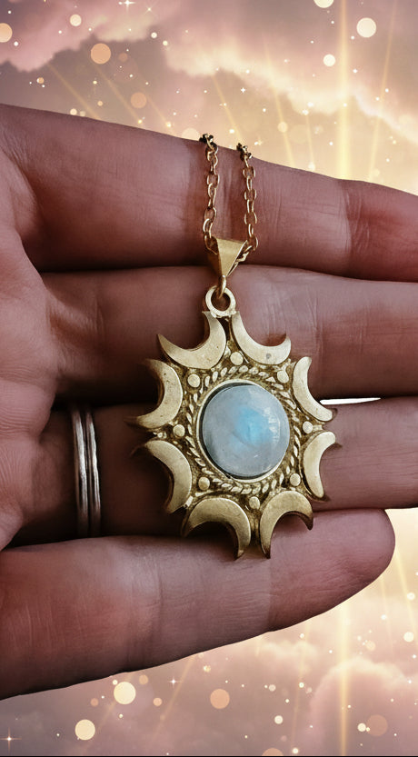 Gold pendant with a central stone held in a hand against a dark background