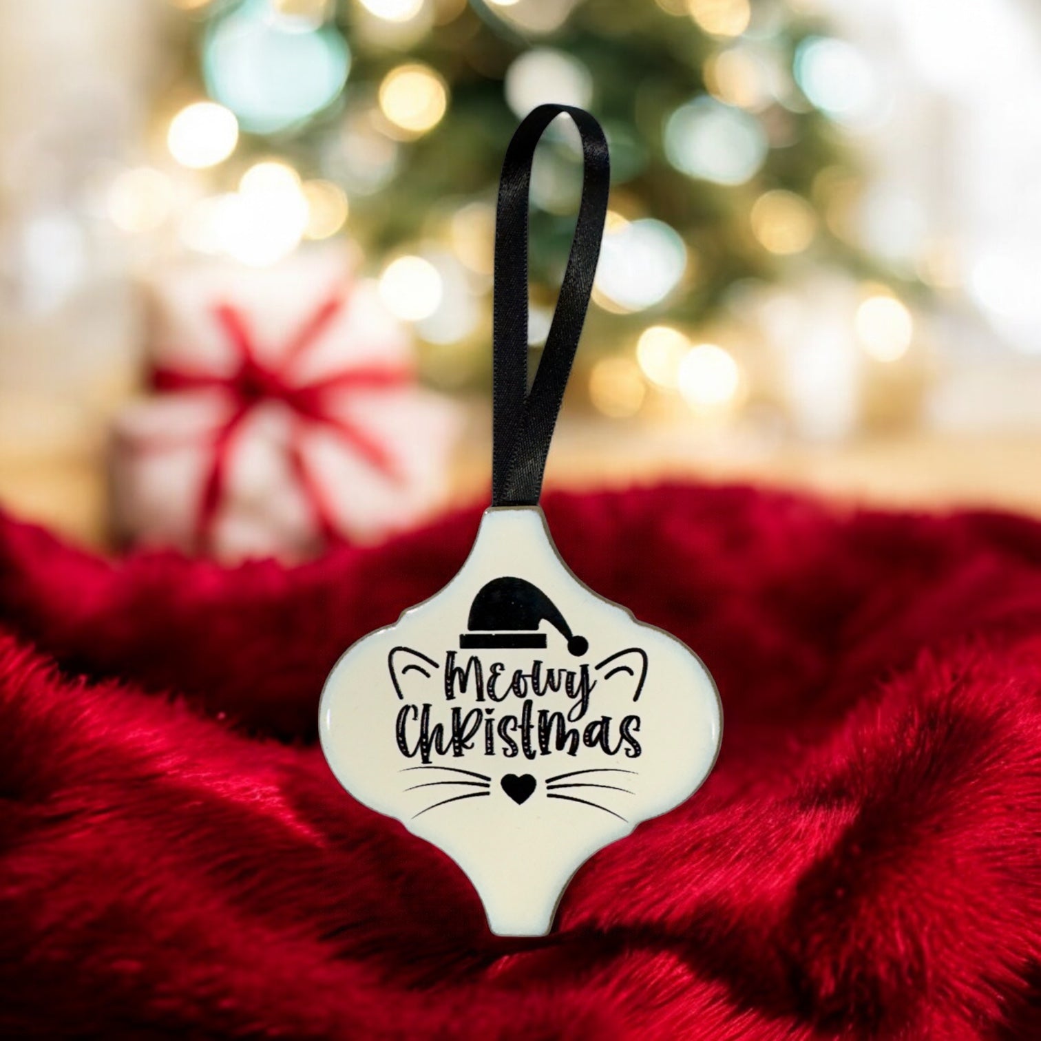 Decorative Christmas ornament with 'Meowy Christmas' text on a red fabric background.
