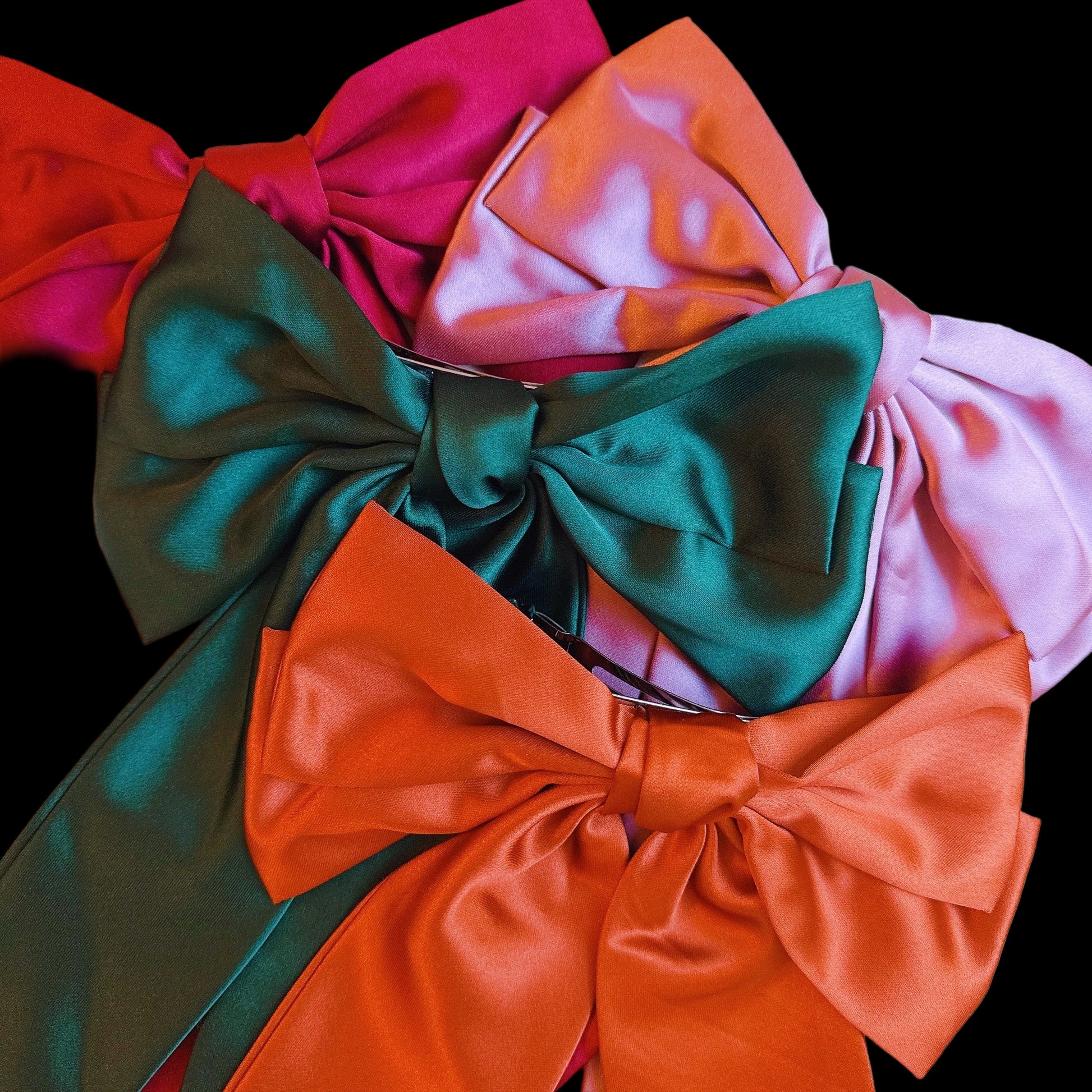 Four large satin bows in red, green, pink, and orange on a white background