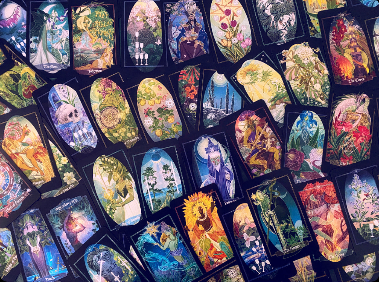 A dense arrangement of illustrated tarot or oracle cards with colorful fantasy and floral artwork, overlapping each other on a dark background.